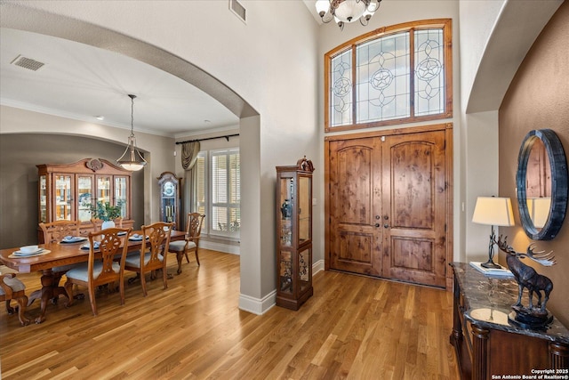 foyer featuring light wood-type flooring, visible vents, arched walkways, and ornamental molding