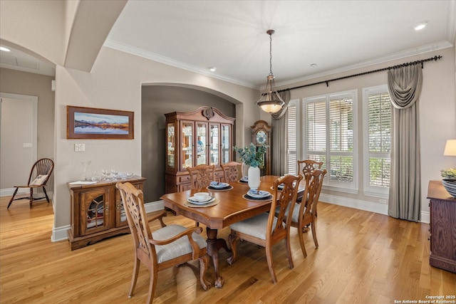 dining room with light wood-style floors, arched walkways, and ornamental molding