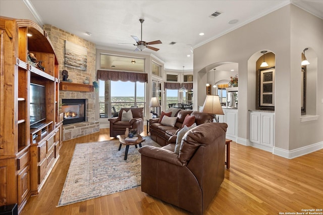 living area featuring crown molding, visible vents, a fireplace, and light wood finished floors