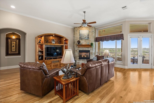 living area featuring visible vents, baseboards, light wood-style flooring, ornamental molding, and a stone fireplace