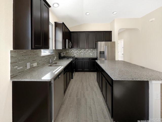 kitchen with decorative backsplash, appliances with stainless steel finishes, a sink, a kitchen island, and light stone countertops