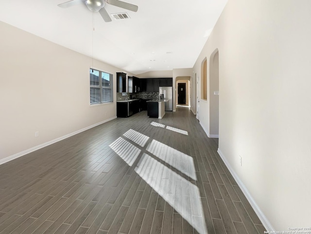 unfurnished living room featuring dark wood-style floors, arched walkways, visible vents, a ceiling fan, and vaulted ceiling