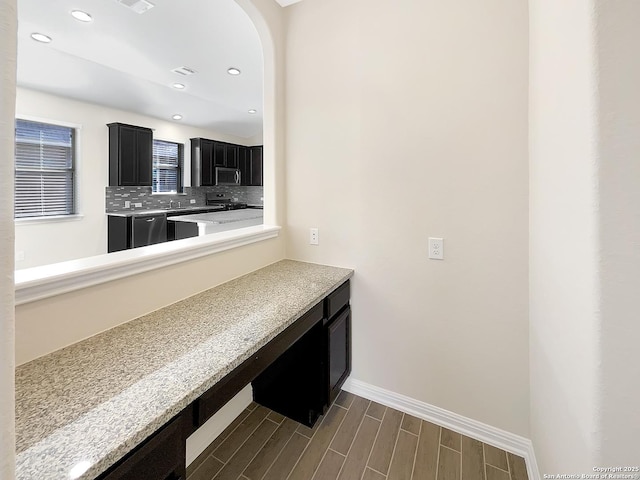 kitchen featuring stainless steel microwave, dark cabinets, light countertops, wood finish floors, and backsplash