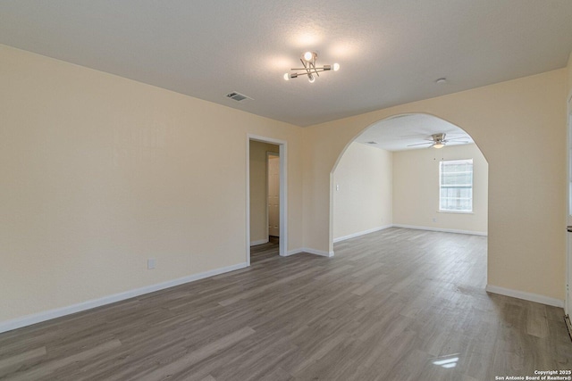 empty room featuring baseboards, visible vents, arched walkways, and wood finished floors