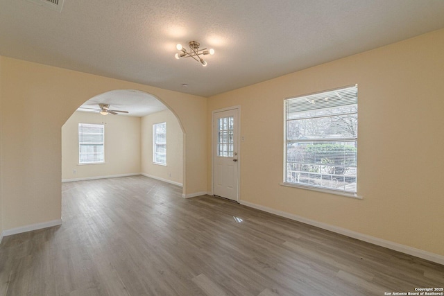 unfurnished room featuring arched walkways, a textured ceiling, wood finished floors, and baseboards