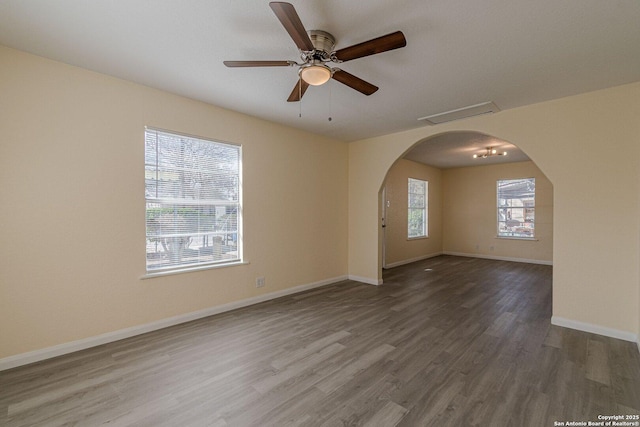 unfurnished room with arched walkways, plenty of natural light, baseboards, and wood finished floors