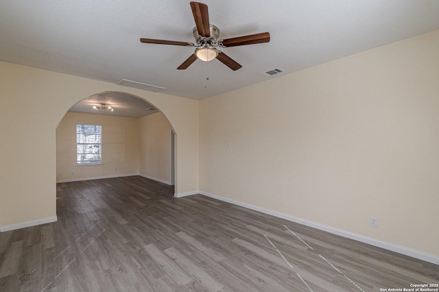 unfurnished room featuring arched walkways, visible vents, ceiling fan, wood finished floors, and baseboards