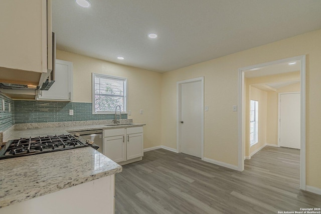 kitchen featuring a sink, white cabinetry, backsplash, dishwasher, and light wood finished floors