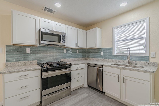 kitchen featuring visible vents, decorative backsplash, stainless steel appliances, white cabinetry, and a sink