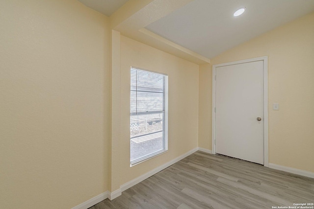 spare room featuring light wood-style floors, baseboards, and vaulted ceiling