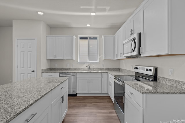 kitchen featuring dark wood-style floors, light stone countertops, stainless steel appliances, white cabinetry, and a sink