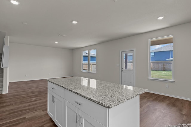 kitchen with white cabinets, dark wood-type flooring, a center island, light stone countertops, and recessed lighting