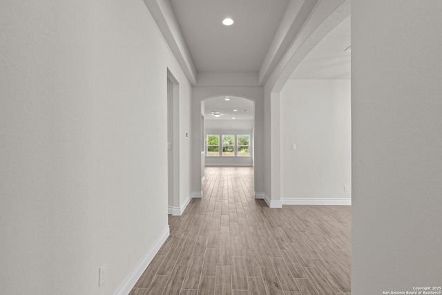 corridor featuring baseboards, arched walkways, wood finished floors, and recessed lighting