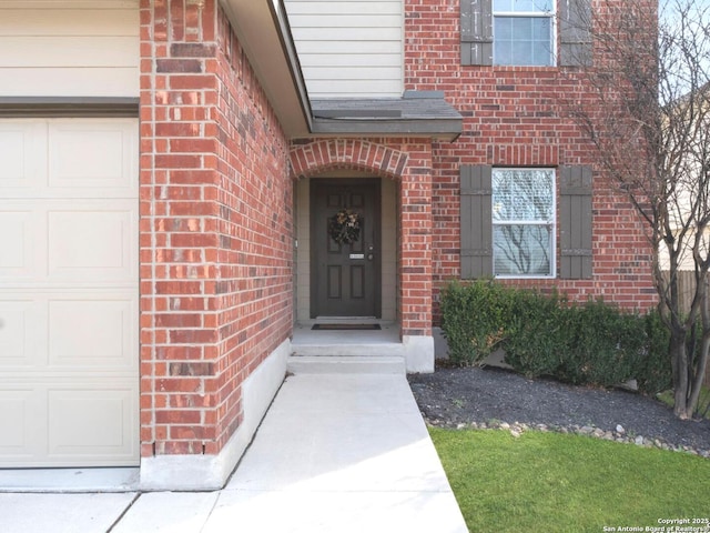 doorway to property with an attached garage, a shingled roof, and brick siding