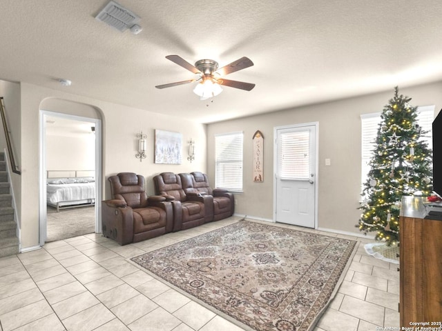 living room featuring a textured ceiling, arched walkways, visible vents, a ceiling fan, and stairs