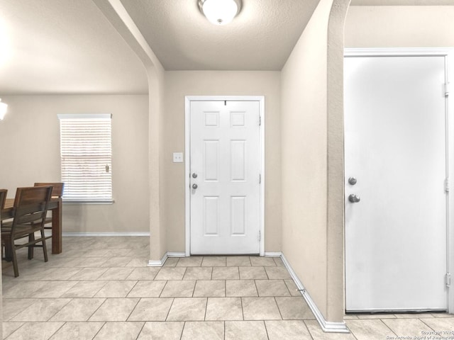 entryway with arched walkways, a textured ceiling, baseboards, and light tile patterned floors