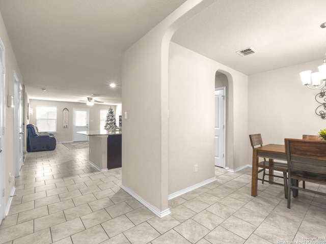 dining area with arched walkways, light tile patterned floors, ceiling fan with notable chandelier, visible vents, and baseboards