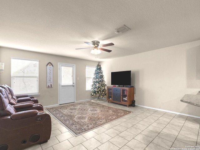 living area featuring light tile patterned floors, visible vents, a ceiling fan, a textured ceiling, and baseboards