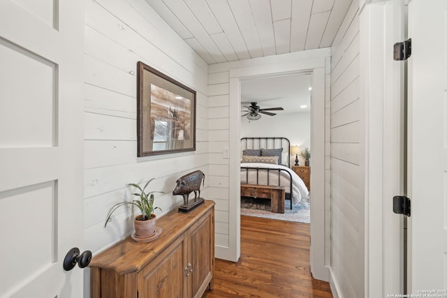 hall with dark wood-style flooring, wood ceiling, and wooden walls