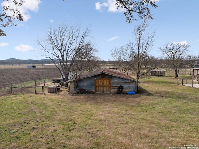 exterior space with a gate, a rural view, fence, and an outbuilding