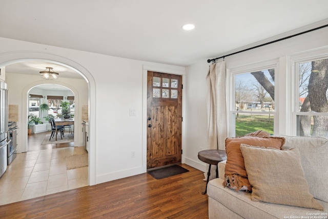 foyer with arched walkways, baseboards, light wood-style flooring, and a healthy amount of sunlight