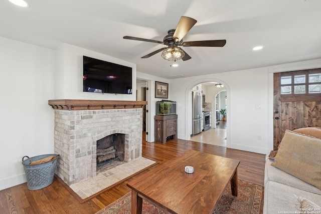 living room with arched walkways, ceiling fan, recessed lighting, wood finished floors, and a brick fireplace