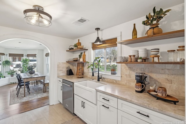 kitchen featuring arched walkways, open shelves, visible vents, stainless steel dishwasher, and a sink