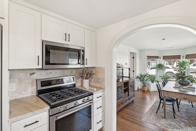 kitchen with arched walkways, stainless steel appliances, wood finished floors, white cabinetry, and light stone countertops