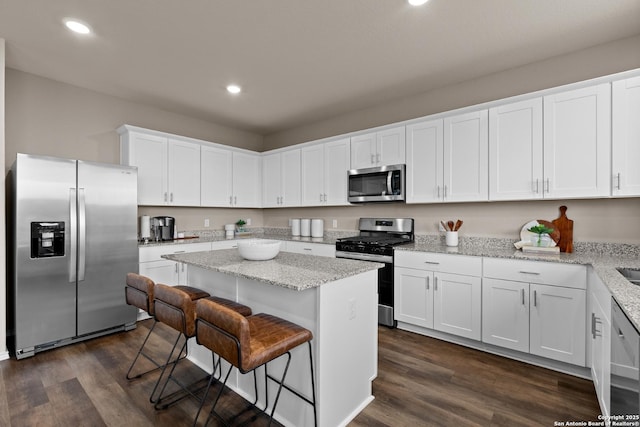 kitchen with a breakfast bar area, a kitchen island, white cabinets, appliances with stainless steel finishes, and dark wood finished floors