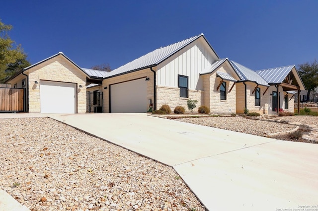 modern farmhouse with driveway, stone siding, metal roof, an attached garage, and board and batten siding