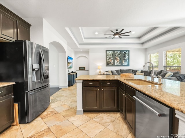 kitchen with open floor plan, a tray ceiling, appliances with stainless steel finishes, arched walkways, and a sink