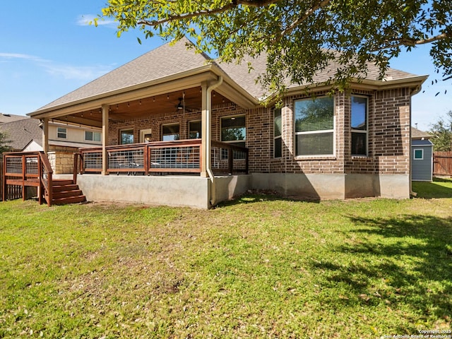 back of house with a lawn, a deck, a ceiling fan, roof with shingles, and brick siding