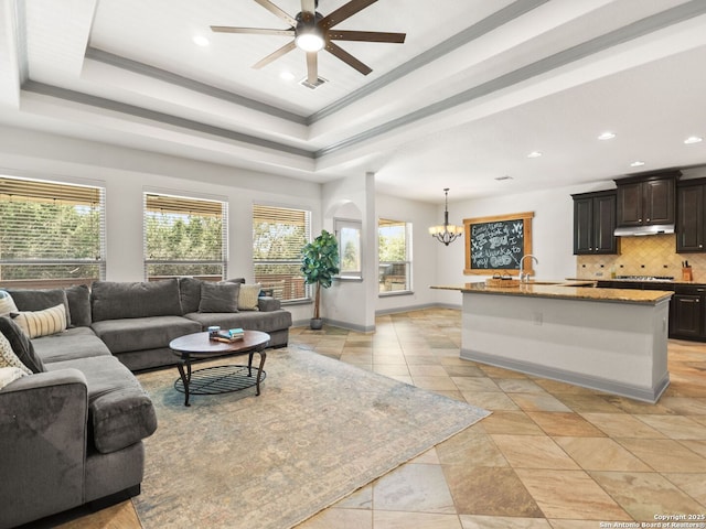 living area with visible vents, a raised ceiling, ceiling fan with notable chandelier, recessed lighting, and baseboards