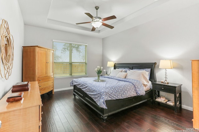 bedroom featuring dark wood-style floors, a tray ceiling, baseboards, and a ceiling fan