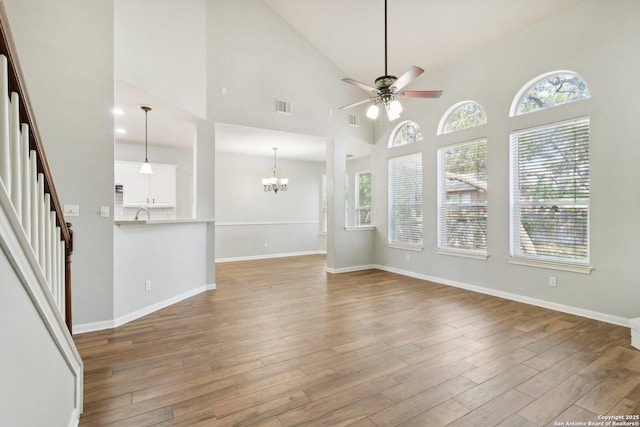 unfurnished living room featuring visible vents, stairway, wood finished floors, baseboards, and ceiling fan with notable chandelier