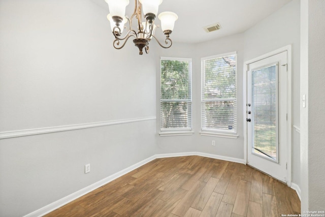 unfurnished dining area featuring an inviting chandelier, visible vents, baseboards, and wood finished floors