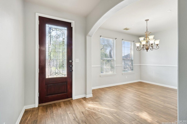 entrance foyer featuring baseboards, visible vents, arched walkways, and wood finished floors