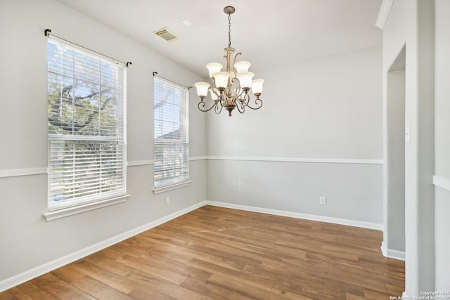 empty room with an inviting chandelier, visible vents, baseboards, and wood finished floors