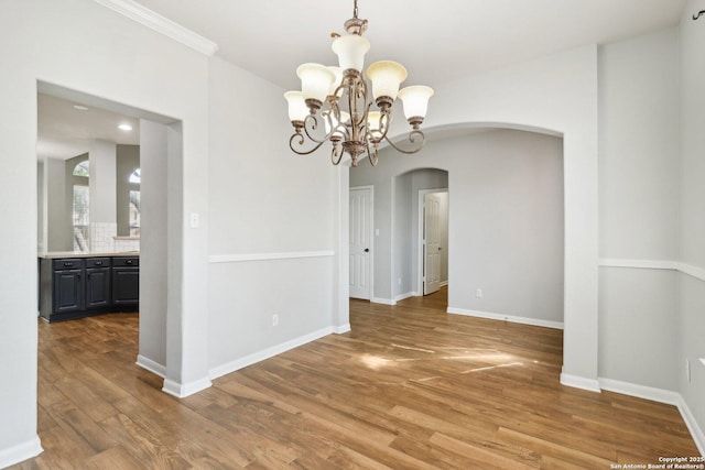 unfurnished dining area featuring arched walkways, baseboards, and wood finished floors