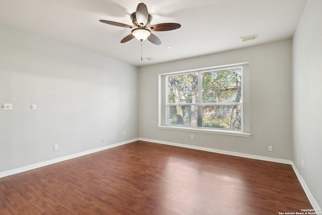 empty room with dark wood-style floors, visible vents, ceiling fan, and baseboards