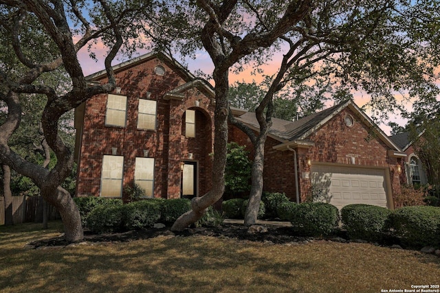 traditional-style house featuring a garage, a yard, and brick siding