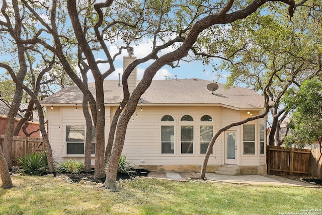 rear view of property with entry steps, a shingled roof, fence, and a lawn