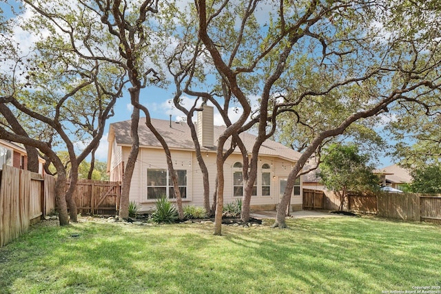 rear view of property featuring a fenced backyard, a lawn, and a chimney