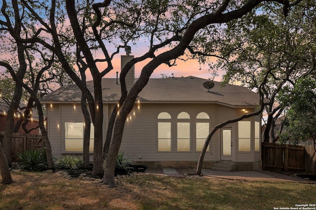 back of house at dusk featuring entry steps, fence, and a yard