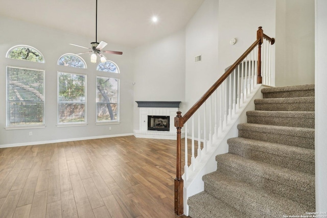 unfurnished living room with a brick fireplace, wood finished floors, high vaulted ceiling, baseboards, and stairs