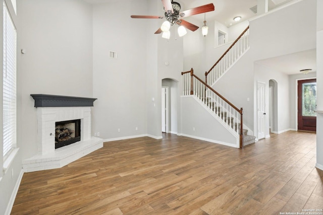 unfurnished living room featuring arched walkways, visible vents, stairway, a brick fireplace, and wood finished floors