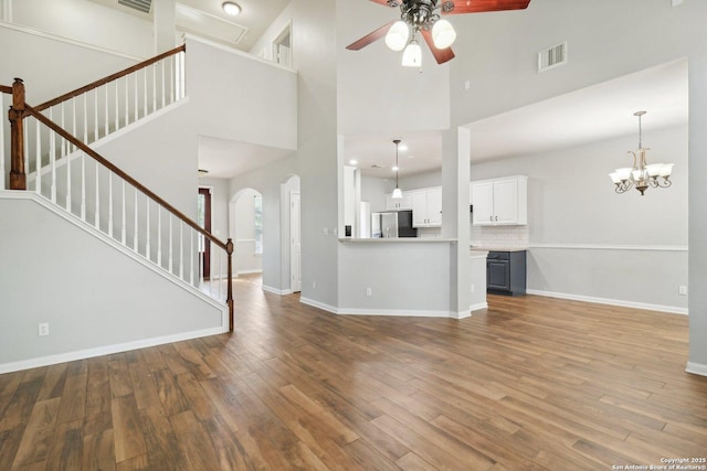 unfurnished living room with visible vents, stairway, wood finished floors, baseboards, and ceiling fan with notable chandelier