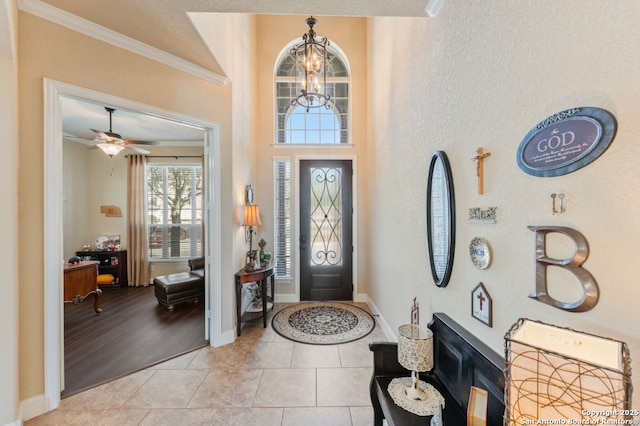 entryway featuring ceiling fan with notable chandelier, ornamental molding, light tile patterned flooring, and baseboards