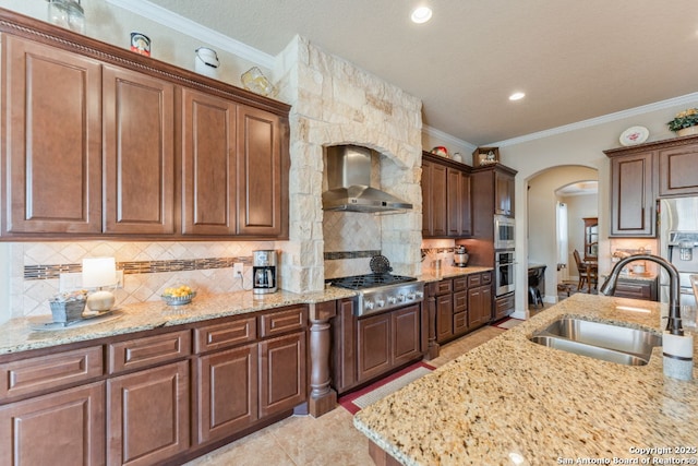 kitchen with arched walkways, a sink, appliances with stainless steel finishes, backsplash, and wall chimney exhaust hood