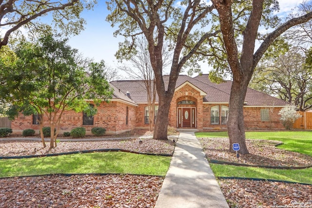 view of front facade with roof with shingles, fence, a front lawn, and brick siding